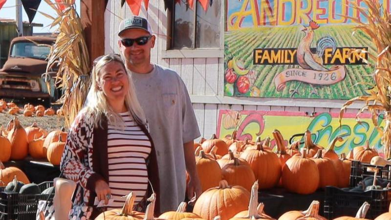 Owners of the Andreotti Family Farm smiling in front of their pumpkin patch.