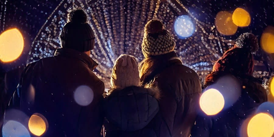 A group of people wearing wooly hats and coats look at a light installation