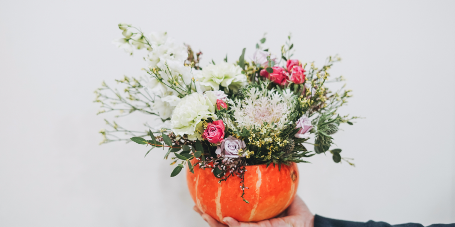 Seasonal floral arrangement displayed in a pumpkin at Ellenborough Park in the Cotswolds, featuring pink flowers and greenery against a light background.
