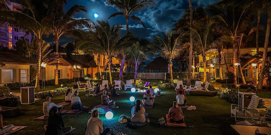 A groupmeditating under a full moon in a grassy courtyard at the Beachcomber Resort and Club. Colorful orbs are interspersed throughout the group