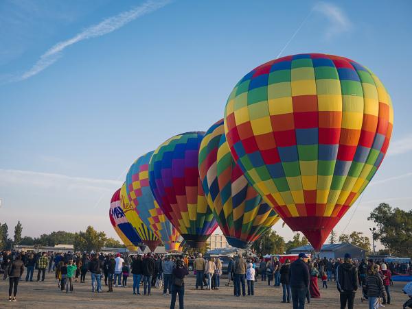 Crowd watching rainbow colored hot air balloons ready for flight