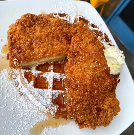 Image of two slices of fried chicken served atop one waffle, covered with maple syrup and powdered sugar.