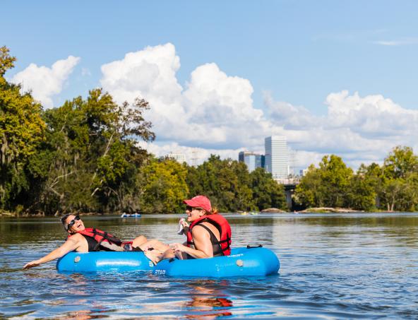 Two people in floats on the river with Columbia skyline in the background