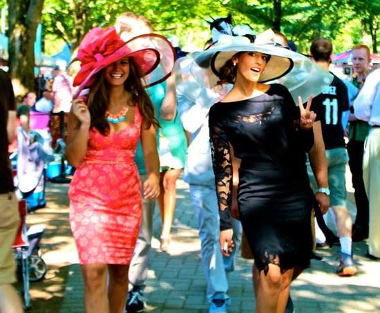 Two women dressed up with large hats at track