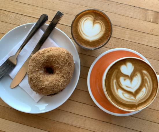View from above of donut on plate next to two cups of coffee topped with artful foam designs at Roosevelt Coffeehouse