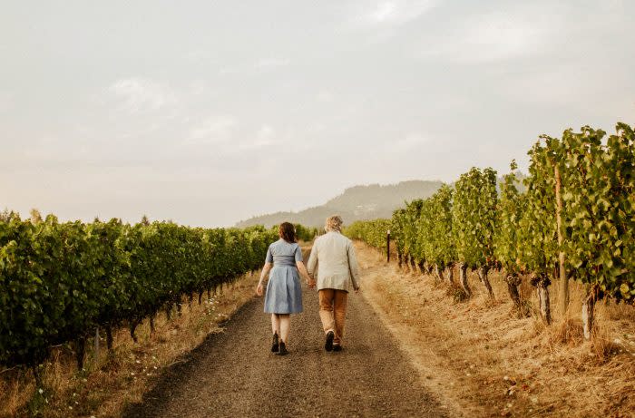 A couple walks down a dirt path through a vineyard