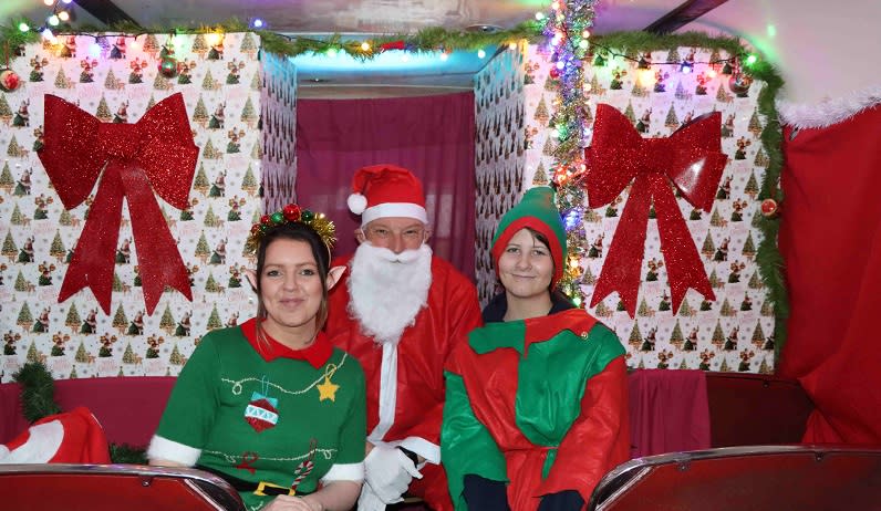Santa and two elves on a Christmas decorated bus