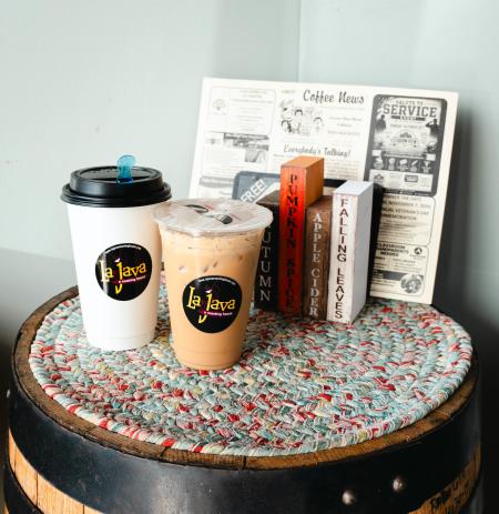LaJava coffee cups filled with fall coffee flavors sit on a rustic barrel table, with festive Halloween decorations in the background.