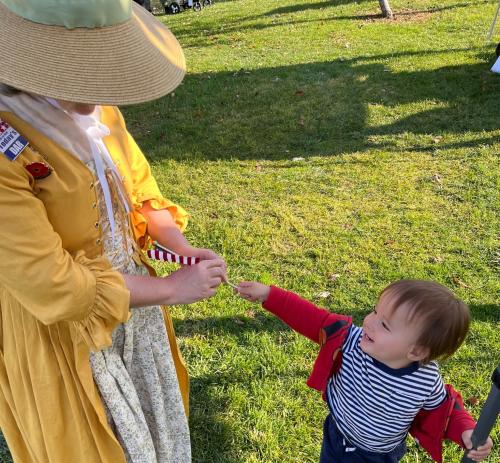 A young child interacts with a woman dressed in 18th century clothing.
