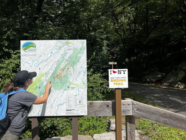 A woman points at a map of the Mohonk Preserve next to an "I BIRD NY" sign