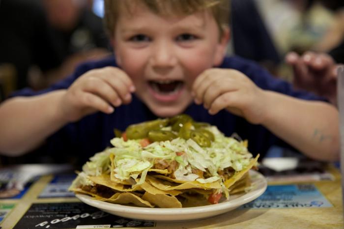 A young boy pretends to take a bite out of a plate of nachos