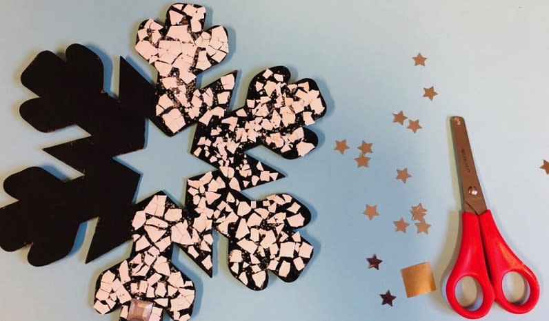 Some scissors and gold stars lie on a table next to a partly-made snowflake mosaic