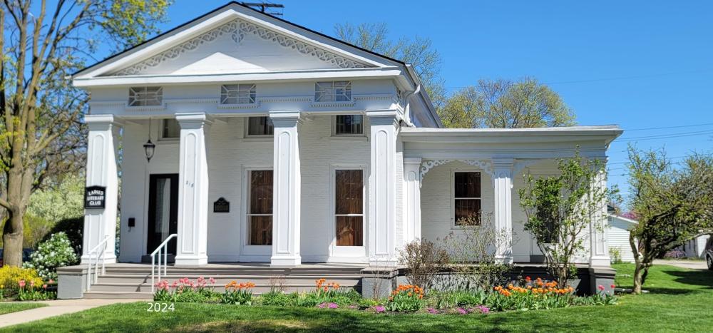 white building with a greek revival architectural style sits on a green grassy site.