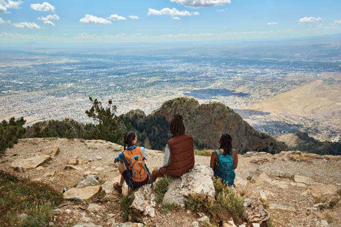 Three people look over Albuquerque while hiking in the Sandia Mountains.