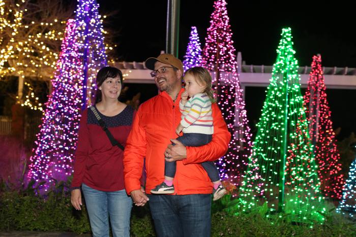 Mom Dad and Daughter walking through christmas trees made of lights