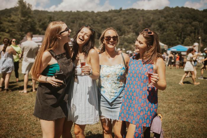 Four girls with small beer glasses laughing with each other at the High Country Fairgrounds.