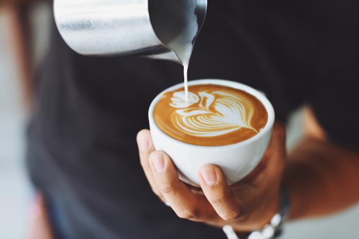 Barista pours cream into mug filled with coffee