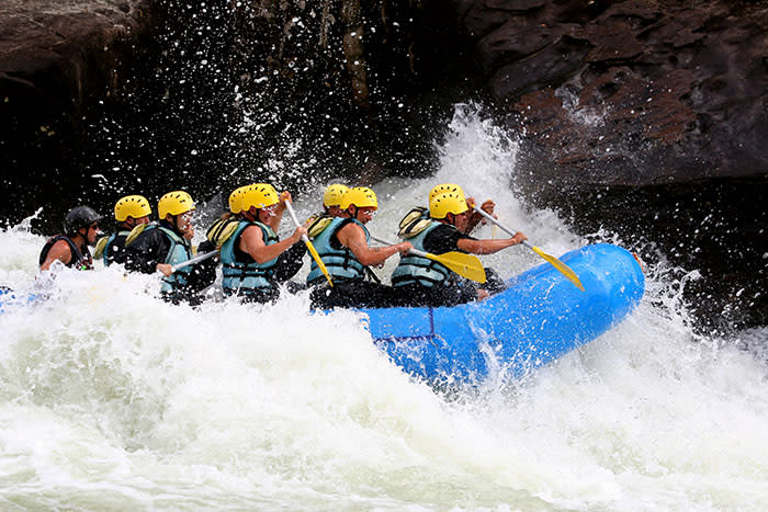 A group of people whitewater rafting in a blue raft with yellow helmets.