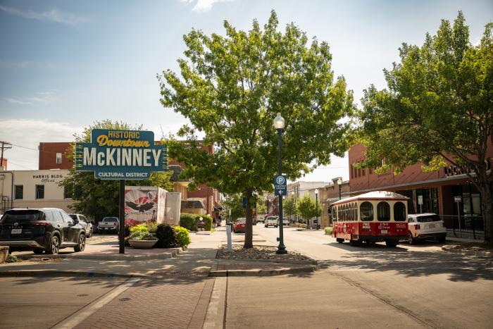 Historical Downtown McKinney welcome sign and red and white trolly on street