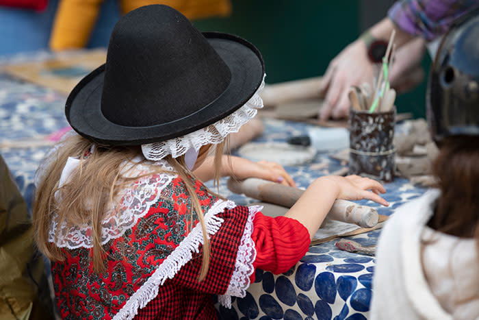 A girl in a Welsh costume rolling craft dough on a table.