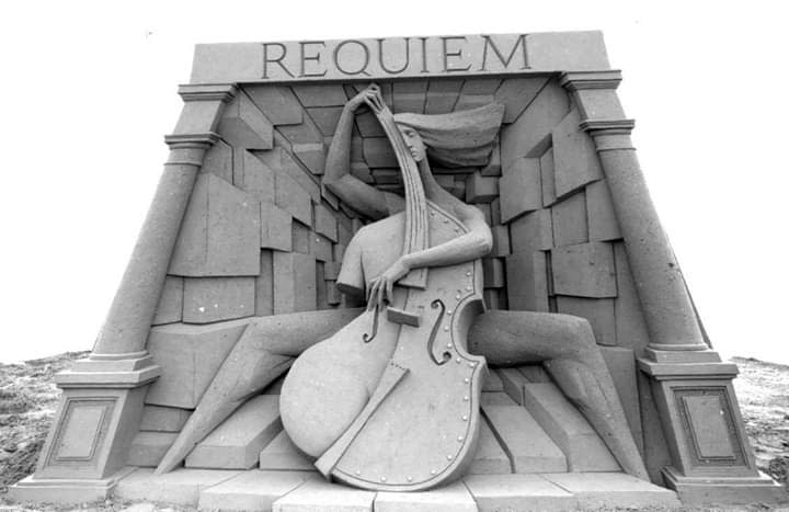 Black and white image of a sand sculpture with the word "Requiem" at the top. Underneath is a woman playing a cello in a hall.