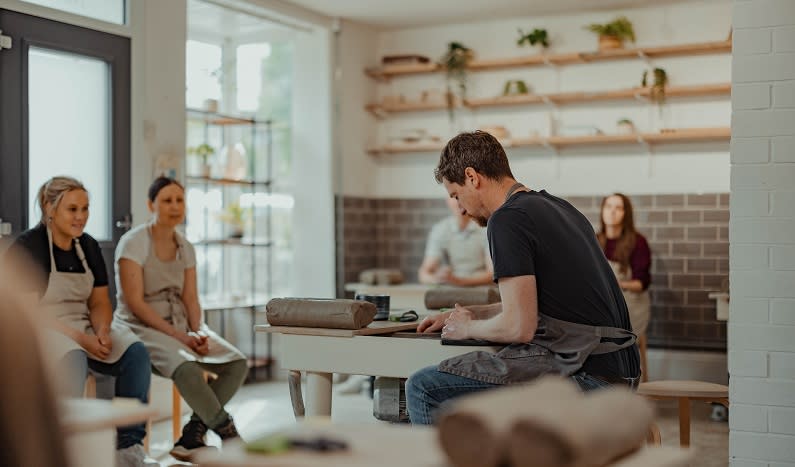 A man demonstrates on a potters wheel for a group of people at a workshop