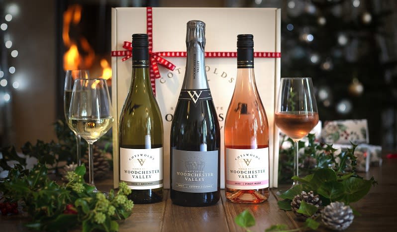 Three bottles of wine and two half-full wine glasses stand on a table decorated with Christmas foliage and infront of a gift box with red bow