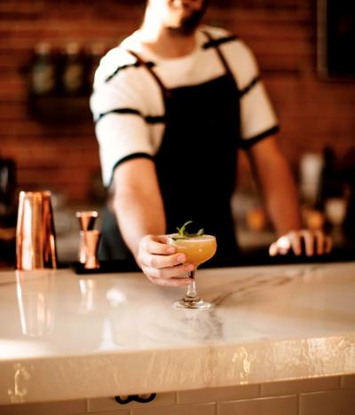 Bartender hands cocktail over counter.