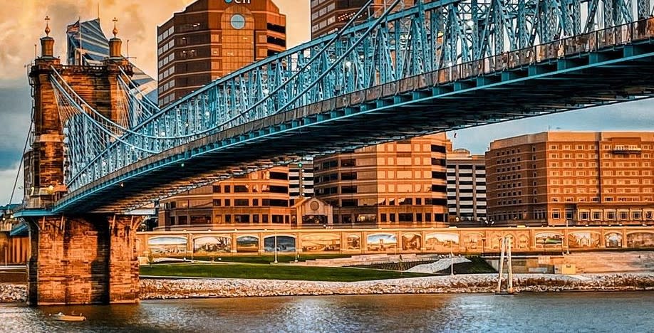 The Roebling Suspension Bridge leading to the NKY Skyline with a row of murals bordering the riverfront