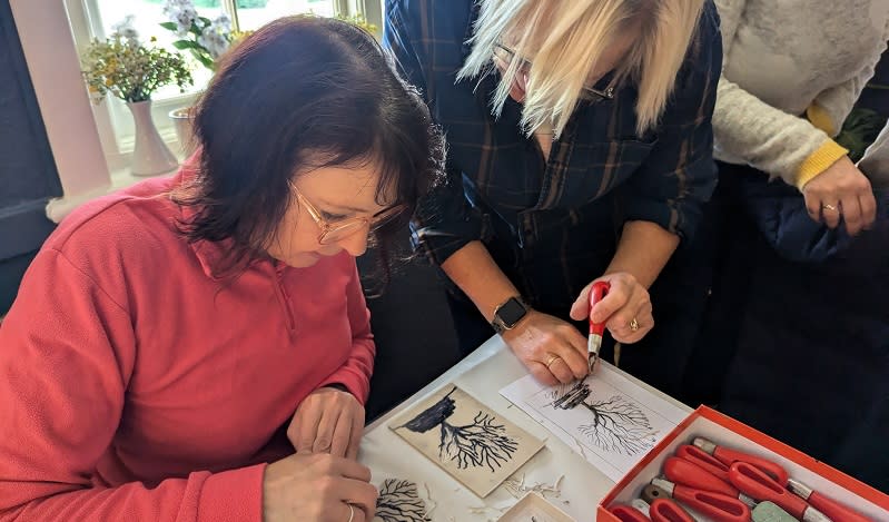 A woman works on her lino print with the help of a workshop leader