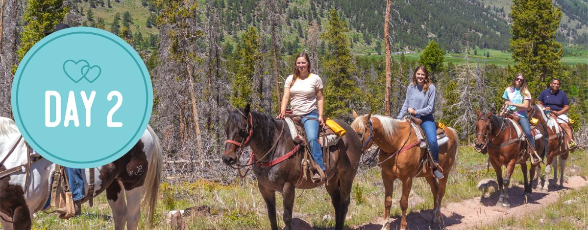 Day 2. People riding horses in a forest on a trail.