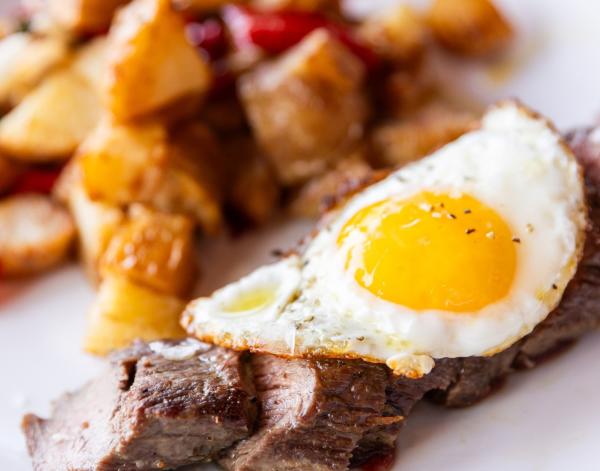 Steak strips with a fried egg on top and breakfast potatoes