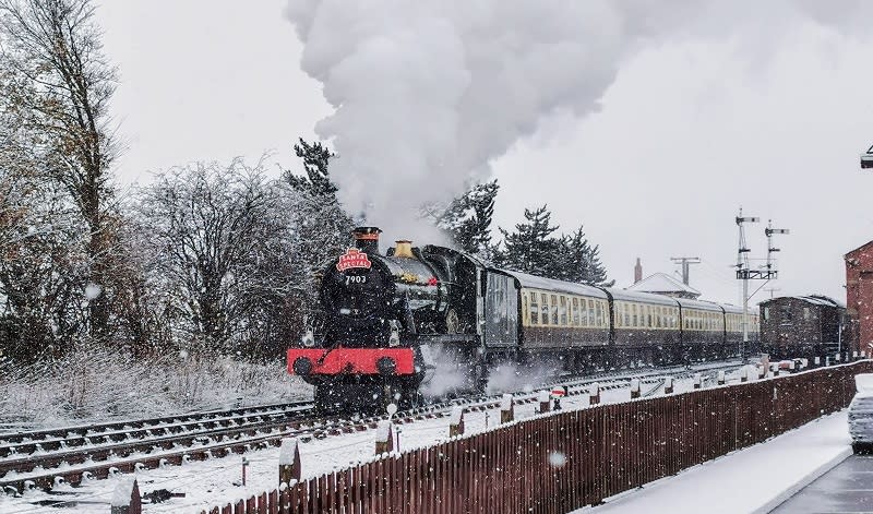 A steam train travels through a snow-dusted station