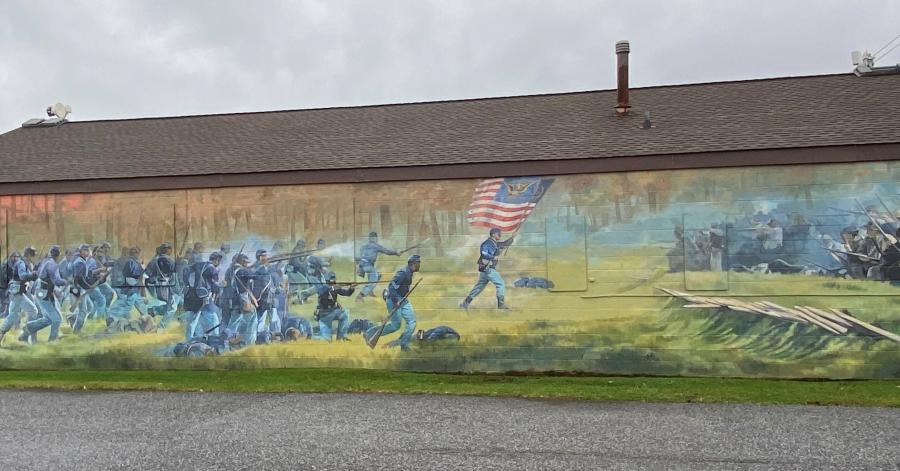 Painted mural of a civil war battle with African American soldiers on side of long building with brown roof