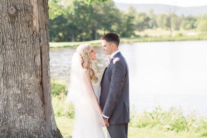 bridge and groom standing beside tree in front of water