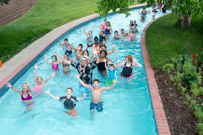 People of all ages in a lazy river with their hands up smiling