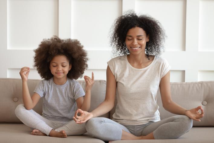African American mother and daughter meditating on a couch