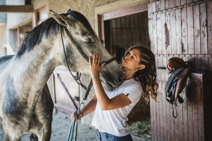 Multi-cultural woman with a grey and white horse in the aisle of a barn