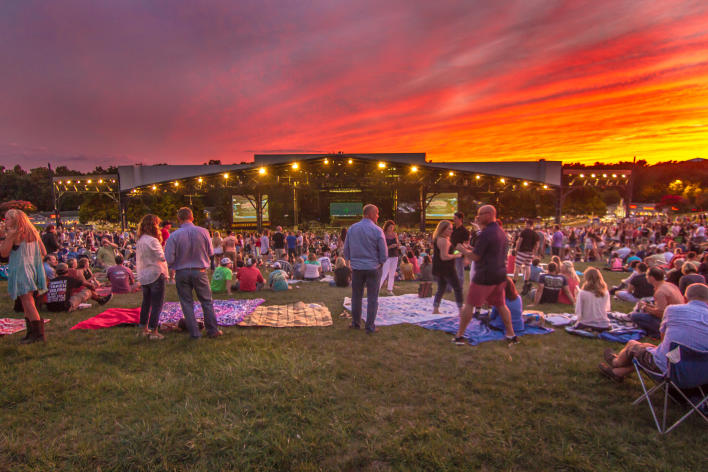 A crowd at an outdoor concert at Jiffy Lube Live at sunset