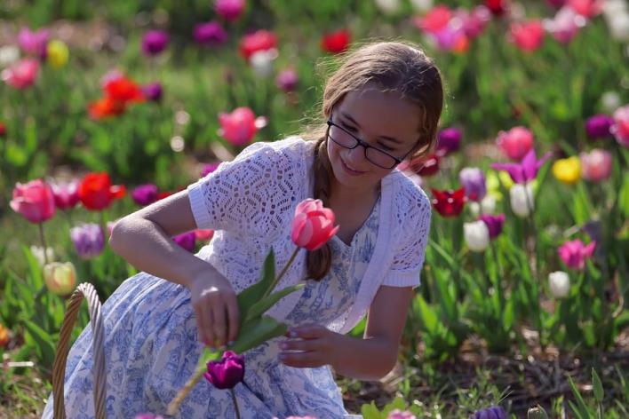 A girl wearing glasses looking at a flower in a field of tulips