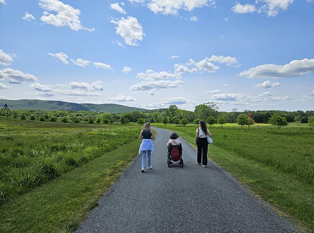 Three people including a person in a power wheelchair on a path surrounded by grassy fields at Storm King Art Center
