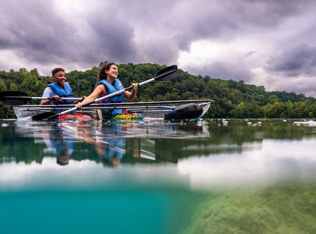 Two people kayaking in crystal kayak on lake