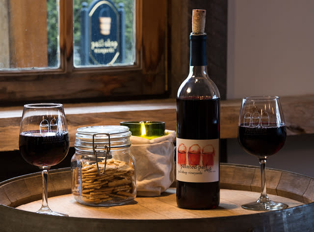 A photo of two wine glasses on a wooden board with a wine bottle and a jar of crackers