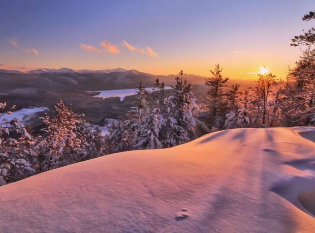 The sun setting over the white snow-covered Adirondack mountain, trees and lakes