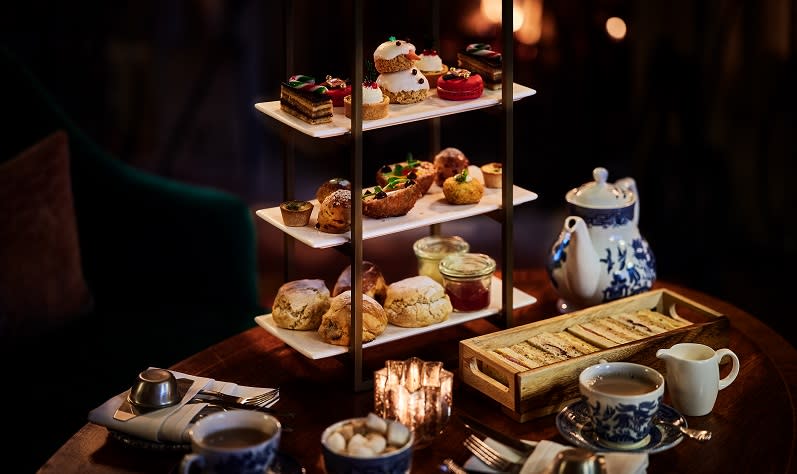 A Christmas themed afternoon tea complete with snowman cake sits on a table infront of an open fire