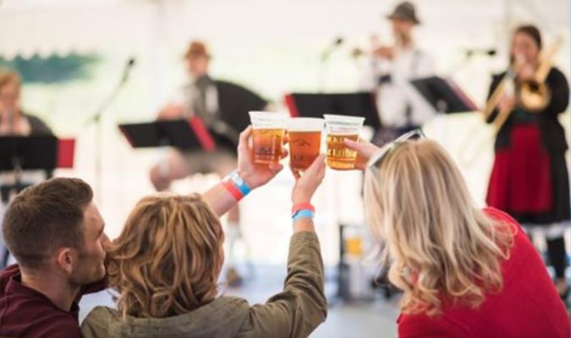 Three people cheers plastic cups full of beer during a live musical performance.