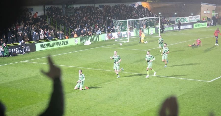 Forest Green Rovers players celebrating a goal on the pitch in front of cheering fans at their home stadium