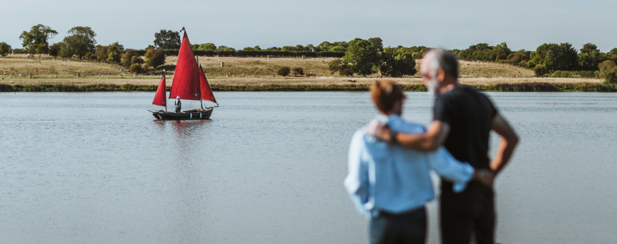 A couple looking out across Hornsea Mere in East Yorkshire as a small boat passes in the distance