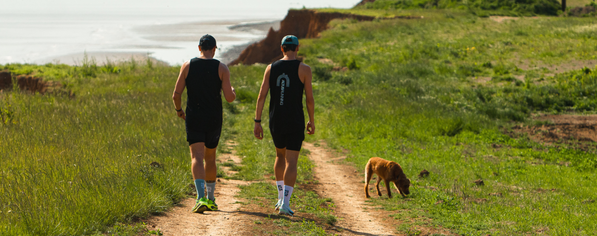 The backs of a couple walking with a dog along a coastal path in East Yorkshire, with the sea ahead of them.