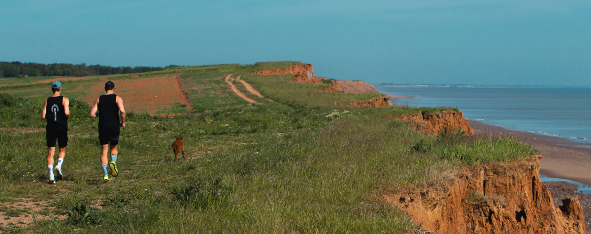 Two runners taking the coastal path with the cliff edge and sea on their right hand side.